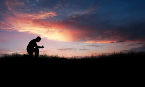 Man in a field watching sunset and meditating